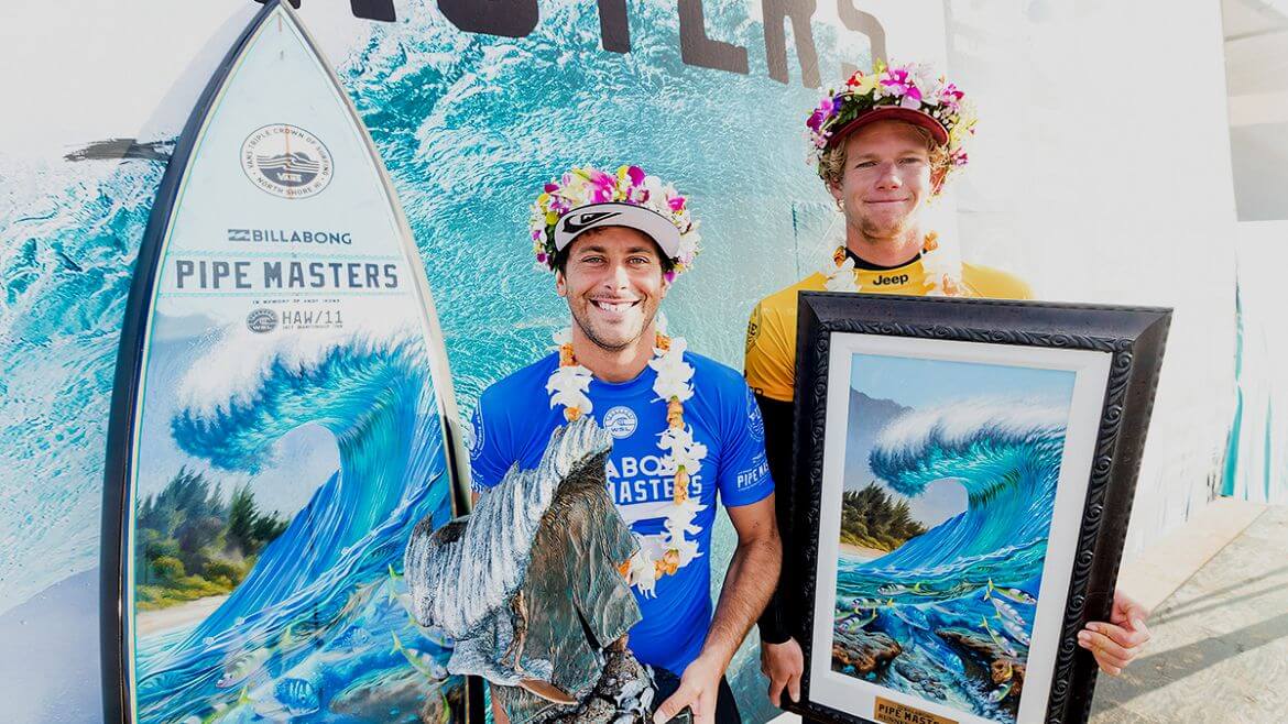 Surfers, Jeremy Flores and John John Florence with the 2017 Pipe Masters surfboard, trophy, and art by Phil Roberts