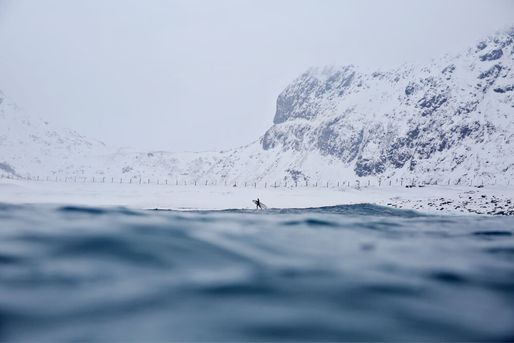 Surfer walking on icy cold beach in snow