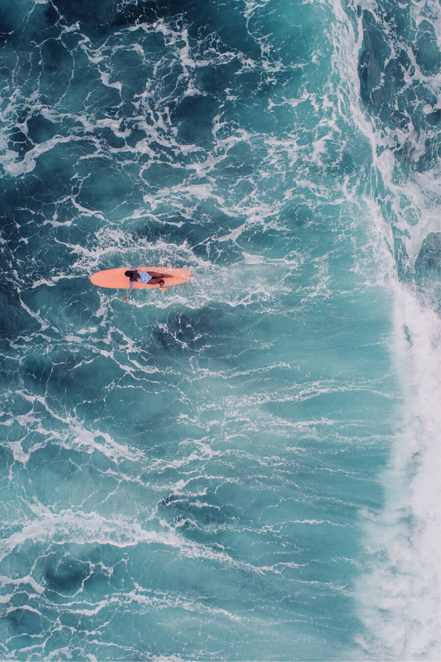 Aerial view of surfer paddling beyond a breaking wave