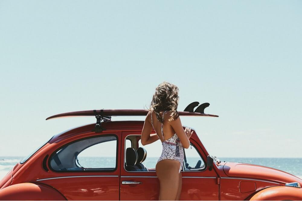 Beautiful woman with beetle car with surfboard on it